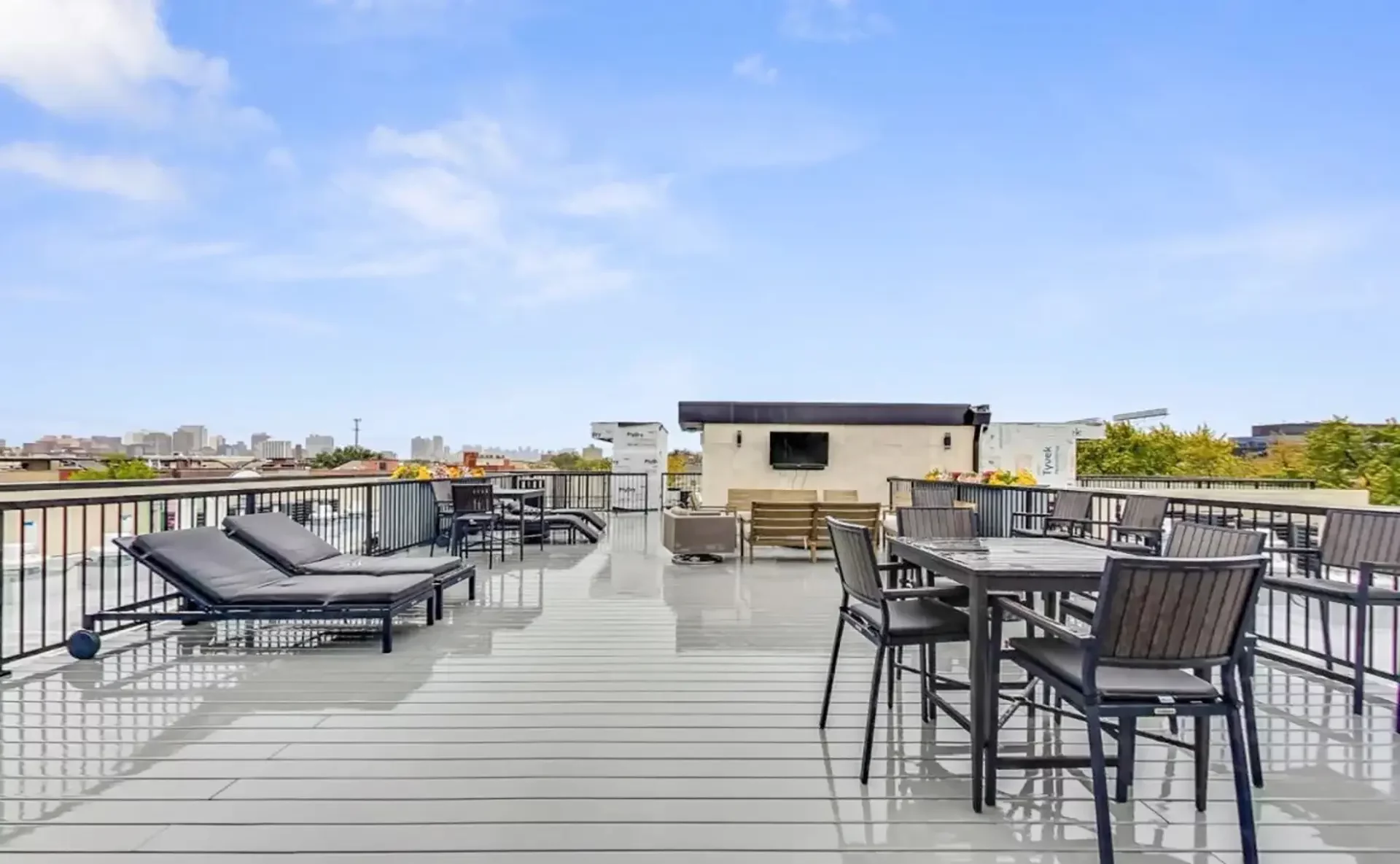 large rooftop patio with lounge seating, table with chairs, and a large television.